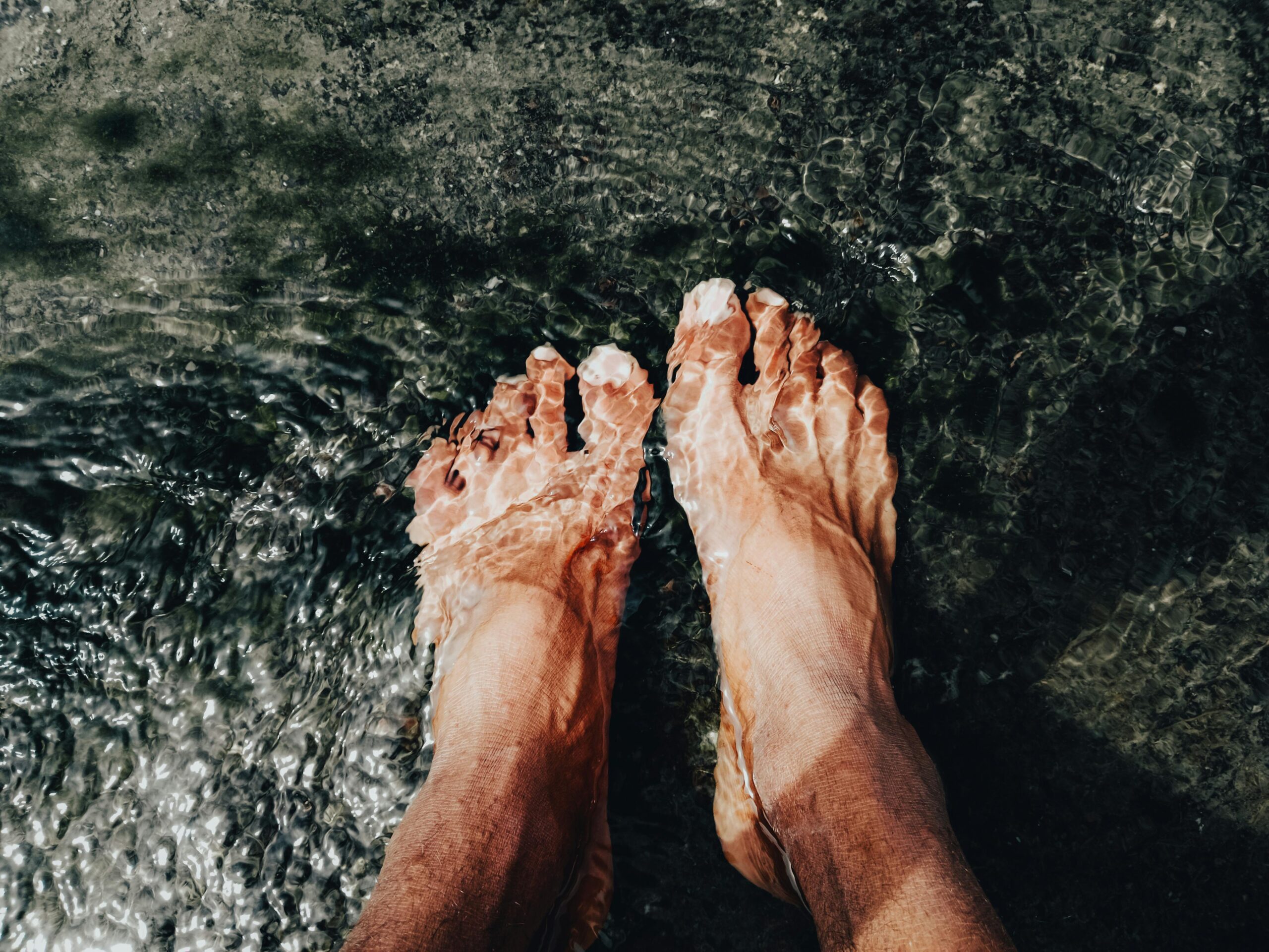 A close-up of feet submerged in clear water, capturing ripples and reflections.