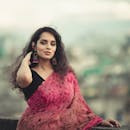 A beautiful South Asian woman wearing a vibrant saree with a blurred cityscape backdrop.
